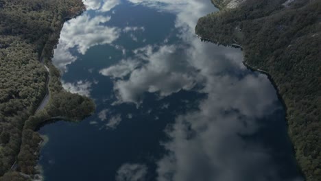 Perfect-cloud-reflection-on-lake-water-surface-in-mountainous-valley,-leisure-boat-creating-ripples,-aerial