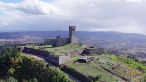 Radicofani-fort-on-hilltop-overlooking-rural-town-in-Italy,-aerial