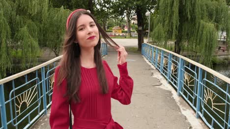 Gorgeous-brunette-in-red-touches-her-hair-and-crossing-bridge-in-the-park