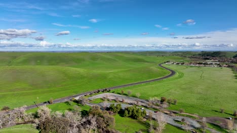 Aerial-view-of-Marsh-Creek-road-winding-through-green-hills-against-blue-sky-Brentwood,-California