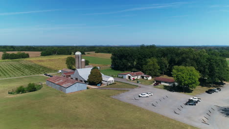 Daytime-aerial-of-farm-with-barn-and-grain-silos-with-fields-in-background,-4K