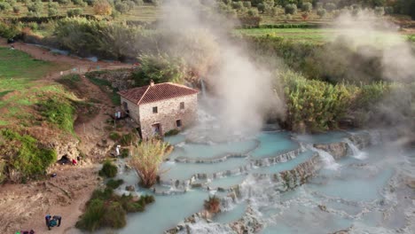 Beautiful-geothermal-hot-spring-with-steam-rising-next-to-old-building-in-Italy,-Saturnia
