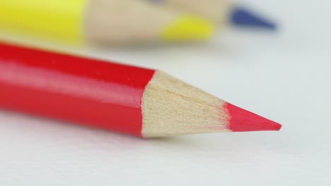 Red-Sharpened-Pencil-On-White,-Yellow-And-Blue-In-Blurry-Background---close-up