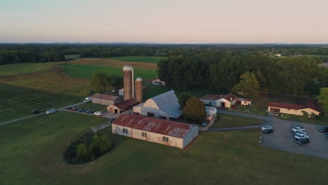 Aerial-view-orbiting-barn-with-grain-silos-at-sunset,-4K