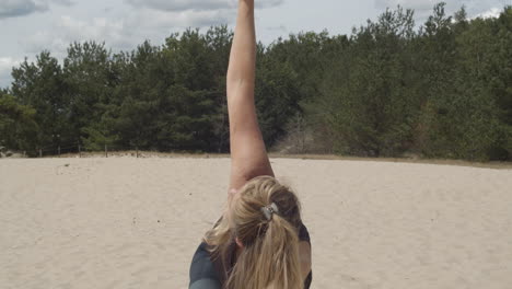 Woman-doing-side-yoga-exercise-in-sand-and-lifting-arm-into-the-air