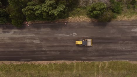 Aerial-top-down-view-of-road-roller,-leveling-sand-and-gravel-during-countryside-road-construction
