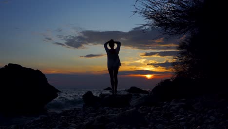 Junge-Frau,-Die-Sich-Am-Felsigen-Ufer-Entspannt-Und-Das-Meer-Unter-Buntem-Himmel-Bei-Sonnenuntergang-Im-Mittelmeer-Beobachtet