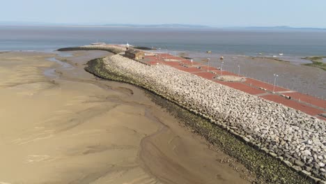 Aerial-pull-back-view-Morecambe-seaside-town-historic-pier-lighthouse-building-low-tide