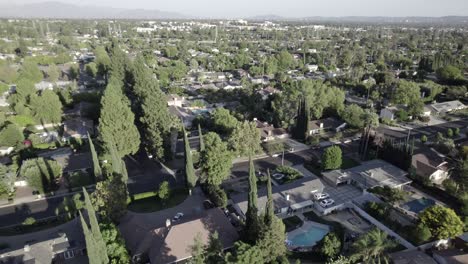 Older-homes-in-Northridge-suburb-neighborhood,-surrounded-by-trees,-aerial-on-clear-afternoon