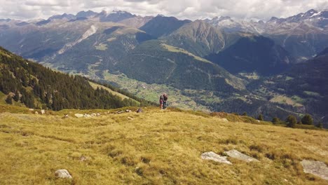 Drone-shot-flying-backwards-of-a-couple-man-and-women-standing-on-a-mountain-looking-over-a-valley-in-Switzerland-in-4k