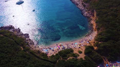 Stunning-drone-shot-of-wild-beach-full-of-sunbathing-people,-umbrellas-and-floating-boats