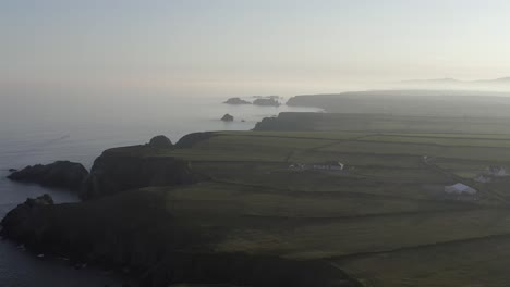 Ethereal-Irish-coastal-cliffs-and-farms-in-misty-morning-fog,-aerial
