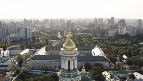 Great-Lavra-Bell-Tower-of-the-ancient-cave-monastery-of-Kiev-Pechersk-Lavra-with-cityscape-background,-Kyiv,-Ukraine---aerial-shot