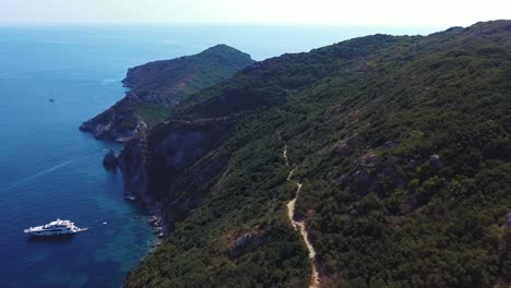 Aerial-shot-of-stunning-hiking-trial-along-the-coastline,-people-are-hiking,-boats-are-floating