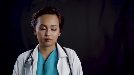 A-female-doctor-or-nurse-looks-at-the-camera-with-copy-space-against-black-background
