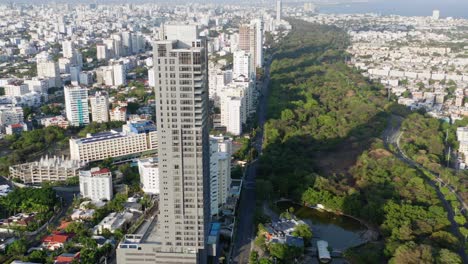Scenic-aerial-view-of-tall-residential-Avenida-Anacaona-skyscraper-and-downtown-Santo-Domingo-city-skyline-and-view-of-ocean-sea-water,-Dominican-Republic,-overhead-drone-descend