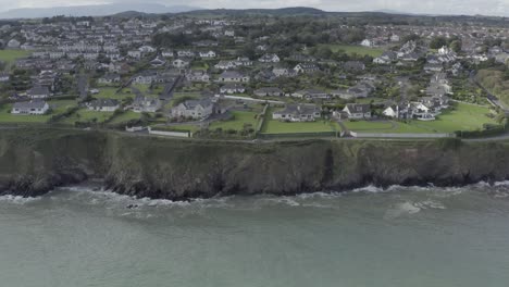 Aerial-flight:-Rocky-seaside-cliff-estates-of-Tramore,-south-Ireland