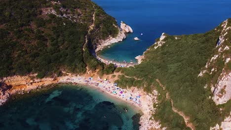 Aerial-cinematic-shot-of-porto-timoni-wild-beach,-sunbathing-people-and-blue-clear-water