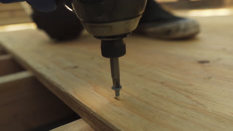 Extreme-close-up-of-a-man-using-a-power-drill-to-insert-a-screw-into-a-sheet-of-plywood-while-building-a-skateboard-ramp