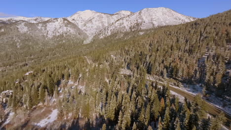 Aerial-of-mountain-landscape-in-Lake-Tahoe,-Nevada,-with-a-pan-to-the-right-to-reveal-a-road-cutting-through-the-trees