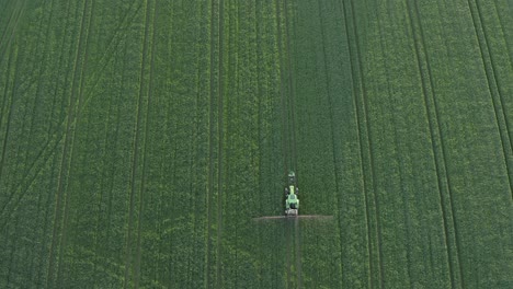 Vertical-aerial-of-vivid-green-crop-field-being-sprayed-by-tractor