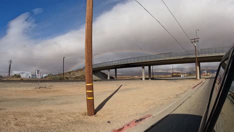 A-rainbow-fills-the-sky-after-a-rare-cloudburst-in-Southern-California's-Mojave-Desert---view-from-a-car-driving-down-the-highway