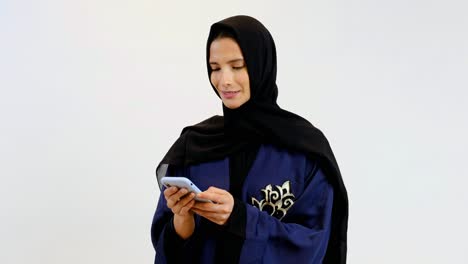 Plano-Medio-De-Una-Mujer-Feliz-Usando-Abaya-Hijab-Usando-Un-Teléfono-Celular-Móvil