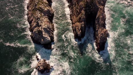 Aerial-top-view-of-waves-breaking-on-rocks-in-a-blue-ocean
