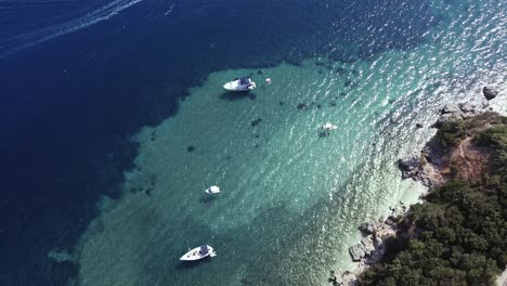 Aerial-shot-of-floating-boats,-blue-clear-water,-small-waves-and-little-island