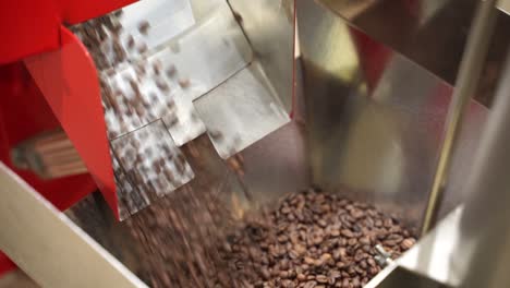 Industrial-machine-pouring-roasted-coffee-beans-in-storage-unit,-handheld-view