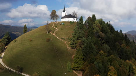 Drohne-In-Richtung-Sveti-Jakob-Kirche-Auf-Grünen-Hügeln-Mit-Touristen-Am-Frühen-Sonnigen-Morgen-In-Slowenien