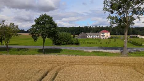 Langsamer-Vorwärtsflug-Aus-Der-Luft-Mit-Leerer-Straße,-Landwirtschaftlichem-Gebäude-Und-Wald-Im-Hintergrund