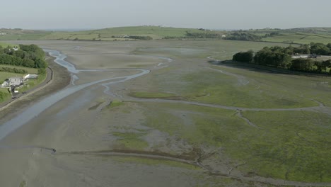 Aerial-view-of-large-mud-flat-lagoon-at-low-tide-and-rolling-farm-land