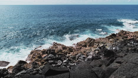 Static-shot-of-blue-ocean-crashing-against-basalt-shoreline-during-sunny-day,slow-motion-shot
