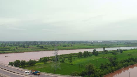Aerial-view-of-the-flyover-over-farming-land-nearby-the-river,-and-the-canal-after-rain-with-rainy-muddy-water-outside-the-city-in-the-Punjab-region,-INDIA