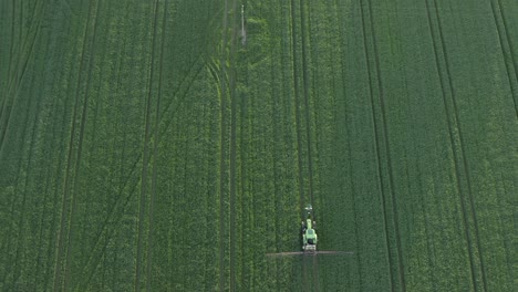 Vertical-aerial-as-tractor-spraying-crop-field-enters-bottom-of-frame