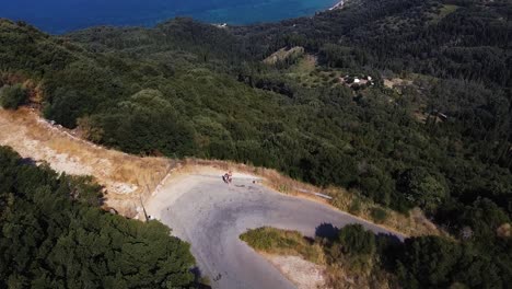 Aerial-shot-of-huge-bay,-lots-of-trees,-winding-road-and-blue-sea-in-Corfu,-Greece