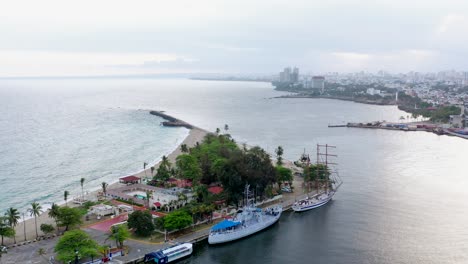 Luftaufnahme-Des-Hafens-Von-Santo-Domingo-Und-Der-Wunderschönen-Punta-Torrecilla-Mit-Hohen-Schiffen,-Die-Am-Hafen-Durch-Ozeanmeerwasser-Angedockt-Sind,-Dominikanische-Republik,-überkopfkreisdrohne