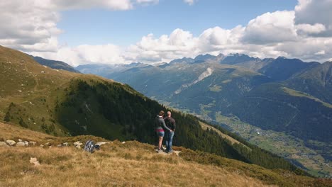 Drone-shot-rotating-behind-a-couple-man-and-woman-standing-on-a-mountain-looking-over-a-valley-in-Switzerland-in-4k