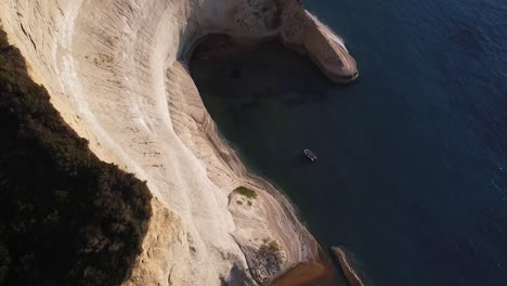 Aerial-shot-of-small-floating-boat-sourounded-by-huge-cliffs-and-calm-sea