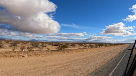 The-Mojave-Desert-as-seen-from-the-car's-side-view-mirror-on-a-day-with-clouds-over-the-barren-wasteland