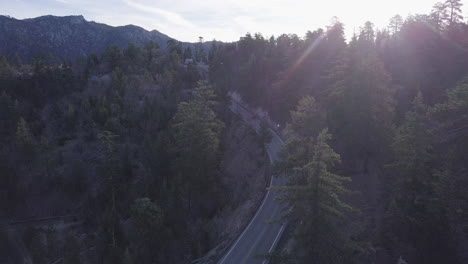 Two-lane-highway-winds-its-way-through-a-mountain-pine-forest-with-a-range-in-the-background
