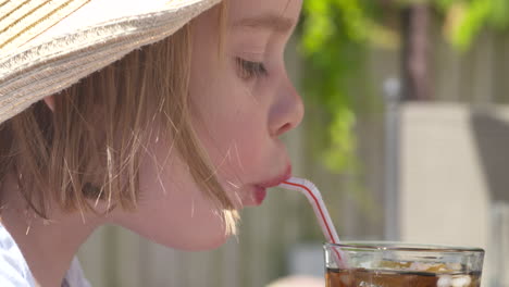 An-adorable-young-girl-taking-a-refreshing-sip-of-cola-outside-on-a-hot-summer-day