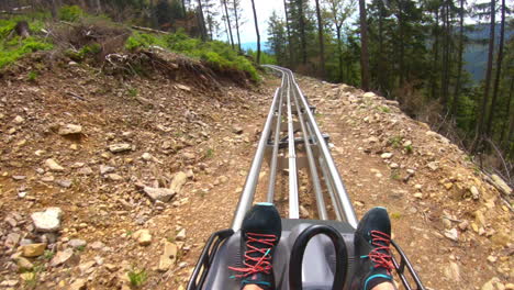 POV-GoPro-shot-of-a-man-riding-on-an-outdoor-roller-coaster-on-a-rocky-mountainside-surrounded-by-trees-in-Dolní-Morava,-Czech-Republic-with-a-view-of-the-countryside