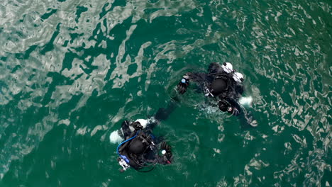 Top-Down-Aerial-View-of-Two-Scuba-Divers-immersing-into-Lake-Waters