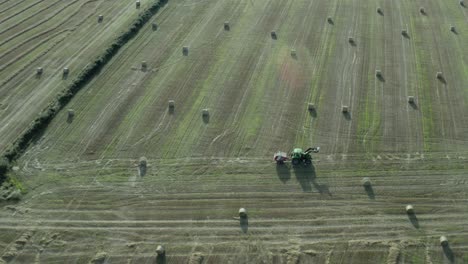 Aerial:-Tractor-with-baler-drives-over-green-hay-field-of-round-bales