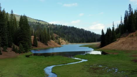 Beautiful-dolly-out-aerial-drone-shot-of-a-stunning-nature-landscape-of-the-Anderson-Meadow-Reservoir-lake-up-Beaver-Canyon-in-Utah-with-large-pine-tree-forest,-a-small-stream,-and-a-grass-field