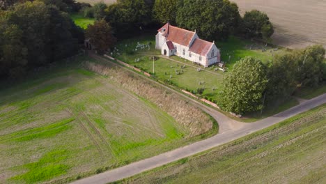 Aerial:-old-village-church-with-cemetery-and-cultivated-agricultural-field---drone-flying-rotation-shot
