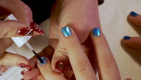 Manicurist-applies-a-clear-coat-polish-to-a-young-girl's-finger-nails---close-up-Christmas-designs