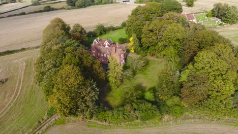 Aerial:-agricultural-farm-land-with-house,-tree-and-cemetery-at-Suffolk,-England---drone-flying-rotation-shot